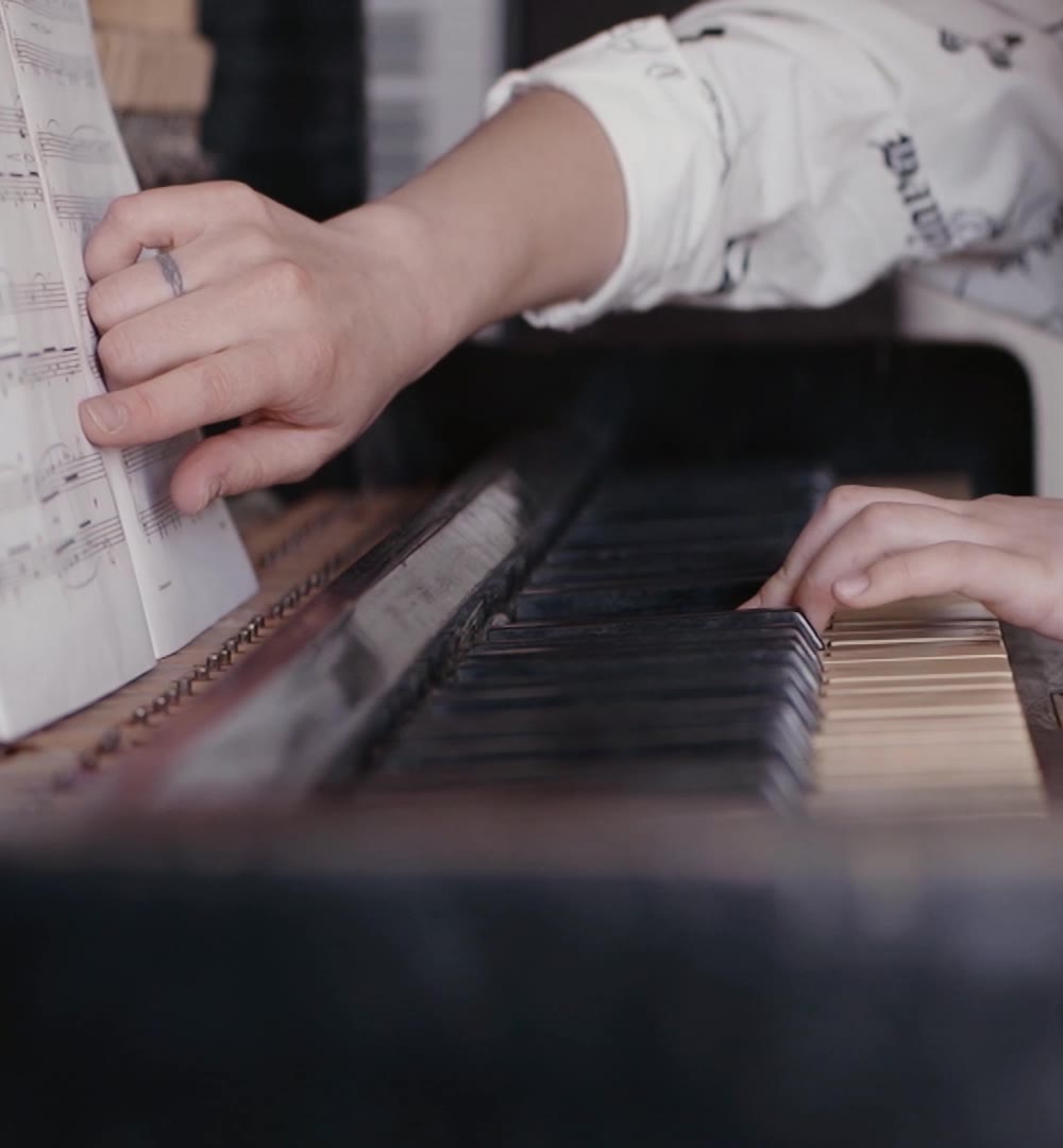 A young student turning a page of sheet music while playing an upright piano